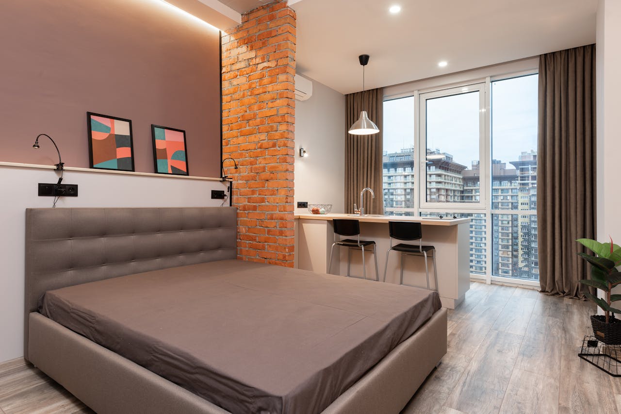 about-01 Modern light apartment interior with bed near counter with chairs near window with curtains and paintings on wall near potted plant